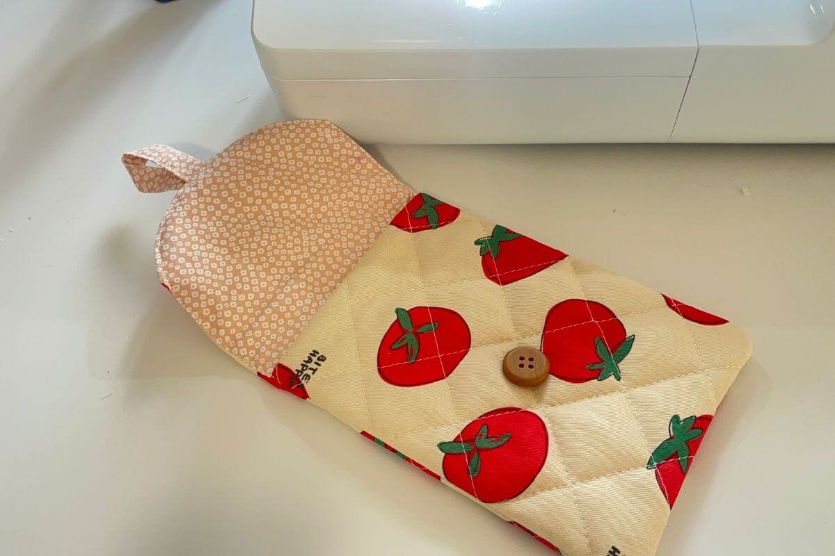 Completed nubim Kindle sleeve with tomato print exterior lying flat with flap open showing the pink floral lining interior and wooden button hand-stitched to the front panel
