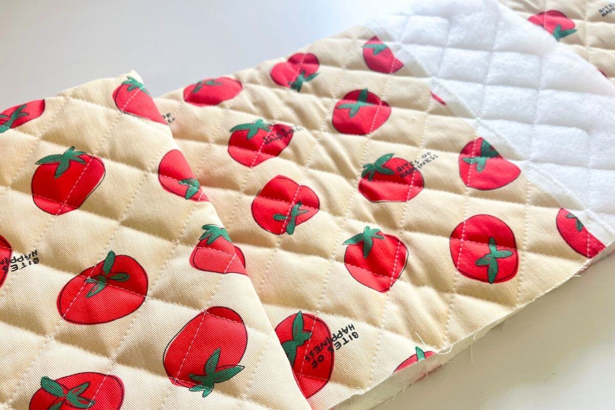 Close-up of tomato print Korean nubim quilted fabric showing the printed outer side overlapping with the white padded reverse side on a white surface
